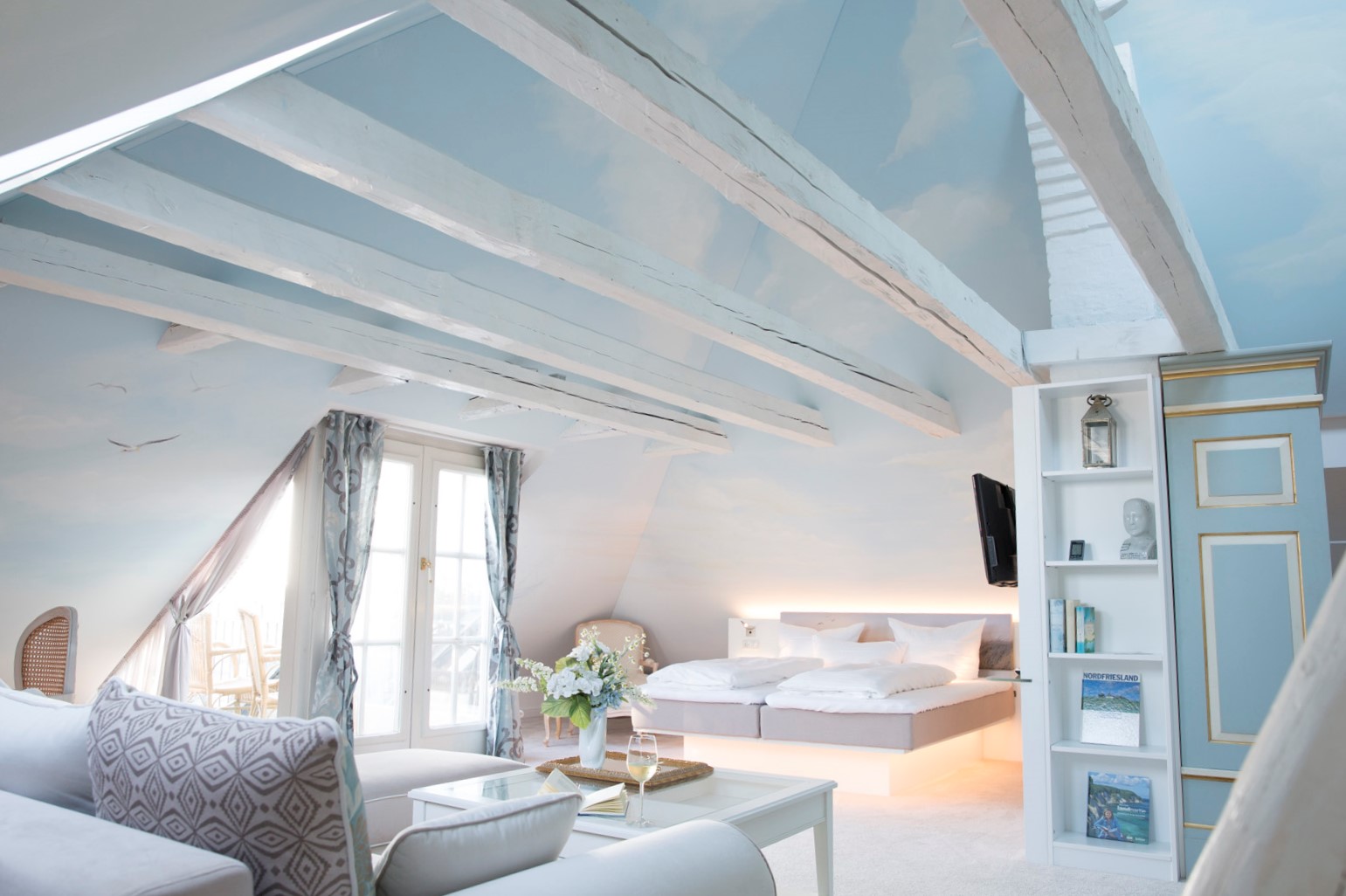 Helles möbliertes Apartment im Dachgeschoss mit weiß getünchten Holzbalken, einem großen Doppelbett und einer Deckenbemalung mit Wolkenmotiv.